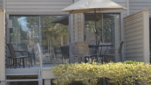A patio with a table and chairs, an umbrella, and a glass enclosure. - 5 Min Walk to Beach- Beach Locker & Chairs, Complete Reno, Golf Green View (Hilton Head Island)