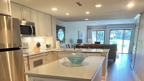 A modern kitchen with stainless steel appliances, a central island, and a view of the living area. - 5 Min Walk to Beach- Beach Locker & Chairs, Complete Reno, Golf Green View (Hilton Head Island)