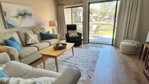 A living room with a sofa, armchair, and a coffee table. There is a painting on the wall and a window with curtains. - 5 Min Walk to Beach- Beach Locker & Chairs, Complete Reno, Golf Green View (Hilton Head Island)