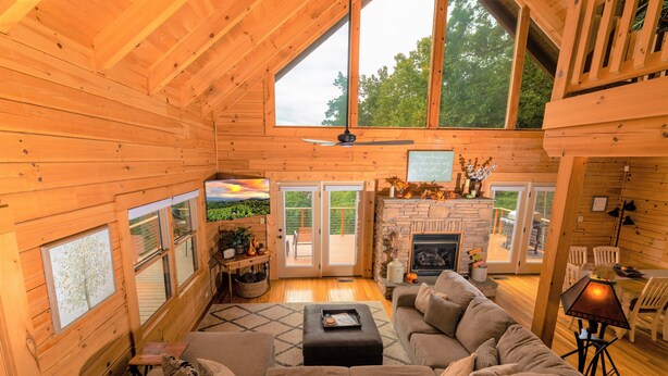 Interior acogedor de una cabaña de madera con un gran techo de madera, chimenea, sofá y comedor.