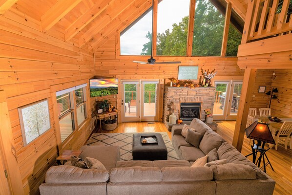 A cozy log cabin interior with a large wooden ceiling, a fireplace, a sofa, and a dining area.