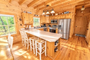 A wooden cabin with a kitchen featuring a large island, bar stools, a microwave, and a refrigerator.