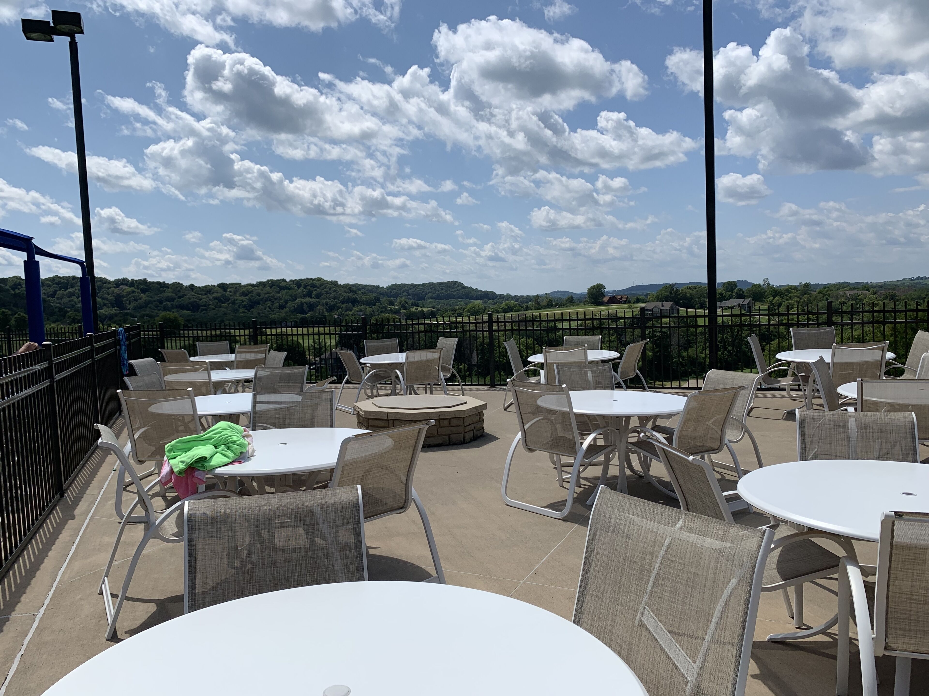 An outdoor patio with round tables and chairs, a view of a green landscape, and a clear sky.
