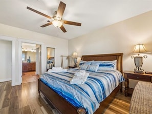 Un dormitorio con cama de madera, ventilador de techo, lámparas de noche y mesita de noche.