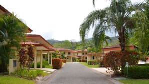 Un camino que lleva a una hilera de edificios de hotel, con un jardín tropical y palmeras.