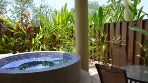 Un jacuzzi rodeado de exuberante follaje, una cerca de madera y una mesa y sillas de vidrio.