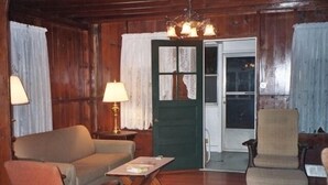 Un salon chaleureux avec un canapé, un fauteuil et une table basse. On y trouve une porte avec un cadre vert et une fenêtre avec des rideaux.