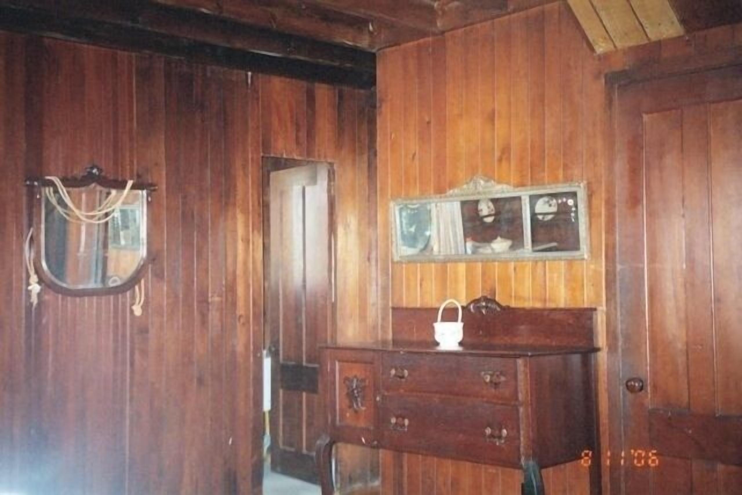 Um quarto de madeira com cômoda, espelho e um quadro na parede.