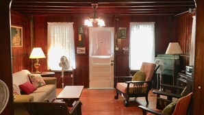 Une pièce chaleureuse avec des murs en bois, une porte blanche, un canapé, un fauteuil, une table et deux ventilateurs.