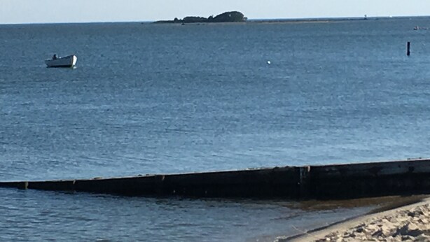 Un paysage côtier avec un bateau sur l’eau, une plage de sable et un promontoire rocheux au loin.