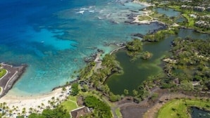 Luftaufnahme eines Küstenresorts mit klarem, blauem Wasser, einem Sandstrand und üppiger Vegetation.