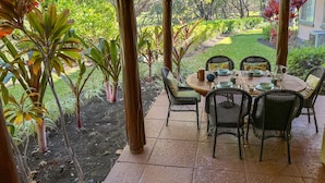 Eine einladende Terrassenanlage mit rundem Tisch und Korbstühlen, umgeben von üppigem Grün und einem gepflegten Garten.