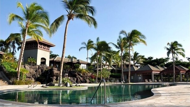 Ein Poolbereich mit Palmen, einer Felsformation und Hotelgebäuden.