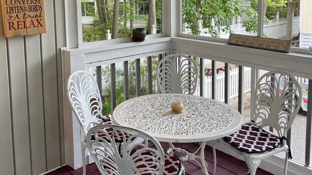 A covered porch with white railings and a table with two chairs. A sign on the wall lists activities like taking a nap and reading a book. - Perfect Key West Style - Golf -Tennis - Pet Friendly (Bethany Beach)