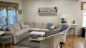 A living room with a sectional sofa, a wicker chair, a small table, and a wall-mounted shelf with the word "BEACH". - Perfect Key West Style - Golf -Tennis - Pet Friendly (Bethany Beach)