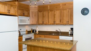 A kitchen with wooden cabinets, a granite countertop, a built-in oven, a microwave, a sink, and two stools. - Lift One - Rustic second floor one bedroom with balcony (Aspen)