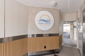 A reception area with a sign for 'Sand Castle 1 Beach Condominium,' a wooden panel design, and a door leading to another space. - 🏖🏝Summer Specials minivans at airports to use (Indian Shores)