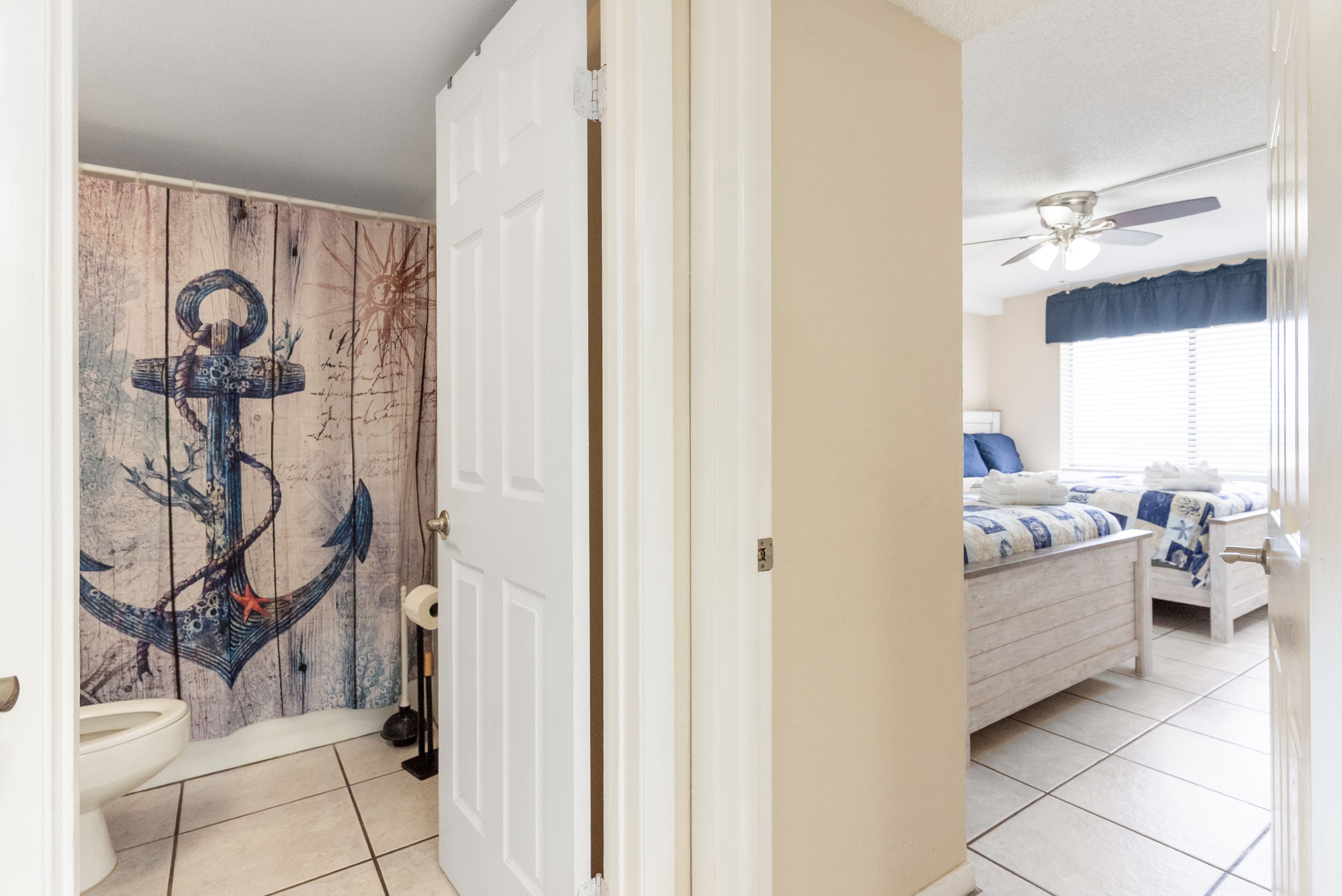 Una habitación con una cama, ventilador de techo y baño con puerta de madera.
