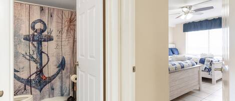 Una habitación con una cama, ventilador de techo y baño con puerta de madera.