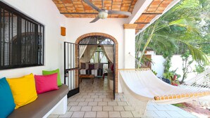 A covered patio area with a hammock, a bench with colorful cushions, and a view of the interior through an open doorway.