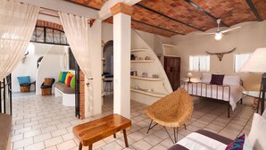 A spacious living area with a sofa, a wooden bench, a wicker chair, and a staircase leading to an upper level.