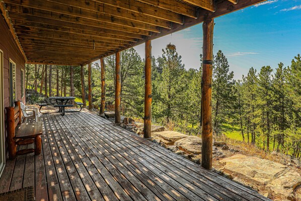 A wooden deck with a picnic table and benches, overlooking a forested area.