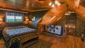 Een slaapkamer met een groot bed, houten plafond en uitzicht op de omgeving door een raam.