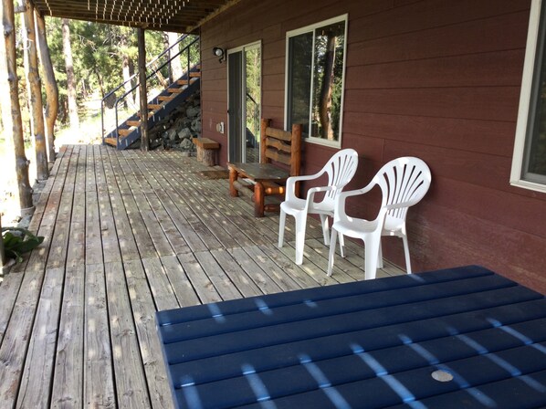 Una terraza de madera con una mesa azul y sillas blancas, una escalera de piedra y un banco de madera.