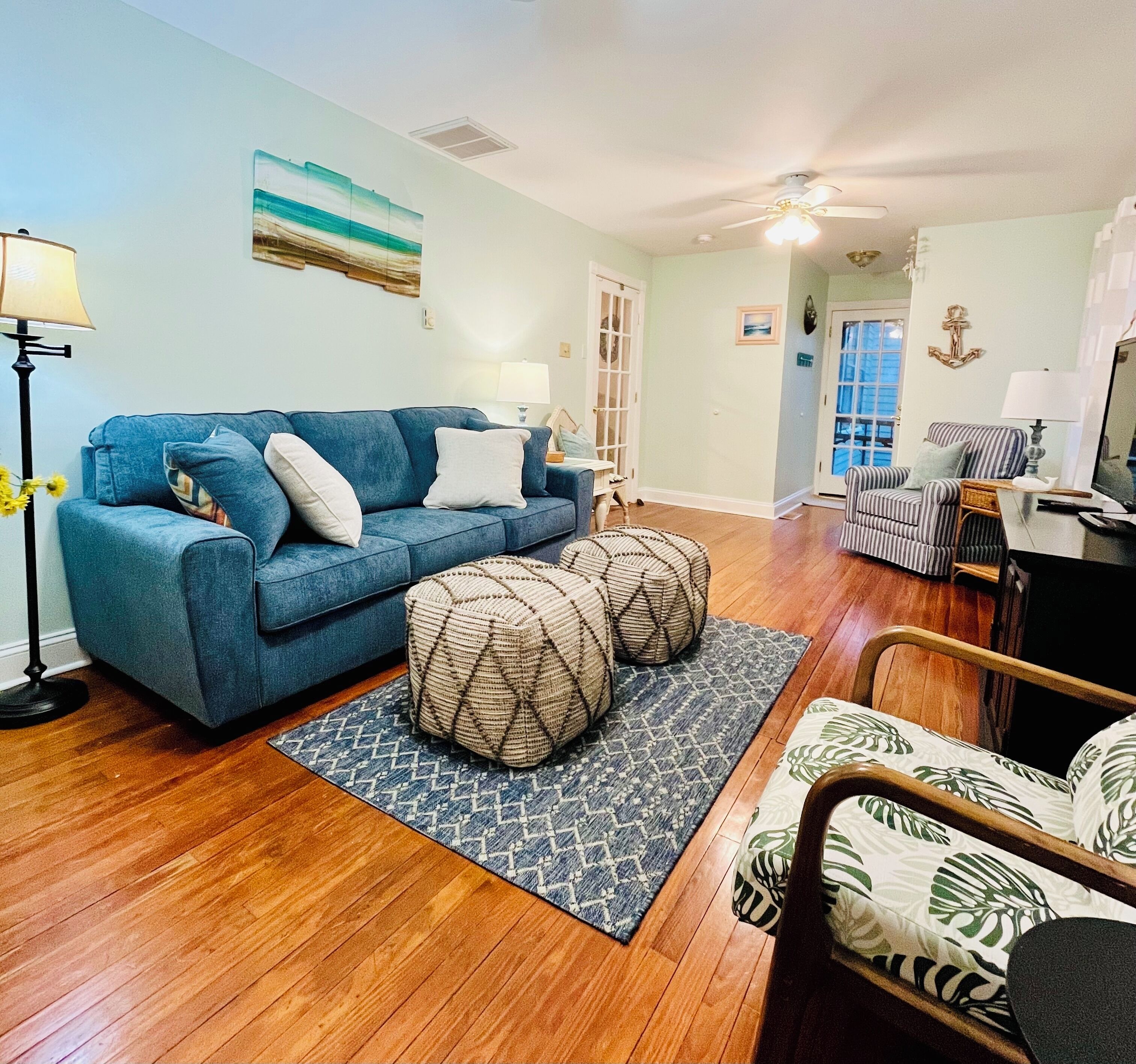 A living room with a blue sofa, two ottomans, a patterned rug, a wooden floor, and a striped armchair.