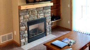 Una sala de estar con chimenea de piedra, televisor montado y una mesa de centro de madera.