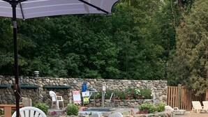 Un patio al aire libre con muro de piedra, piscina y sillas de descanso.