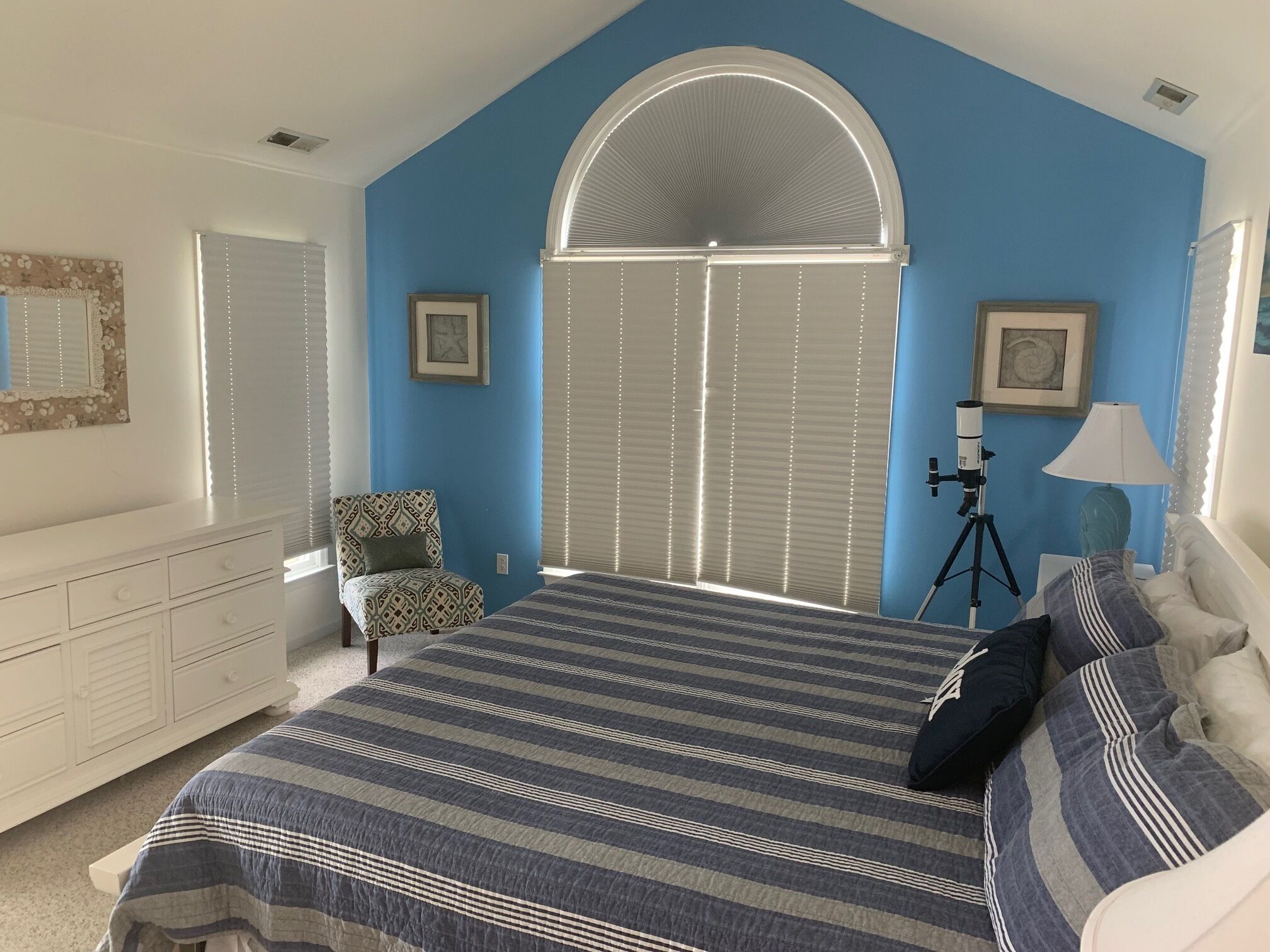 Une chambre à coucher comprenant un lit, une commode, une chaise, un bureau avec une lampe et un télescope.