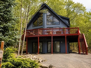 Une cabane moderne à deux étages, dotée d’un balcon rouge et entourée d’arbres.