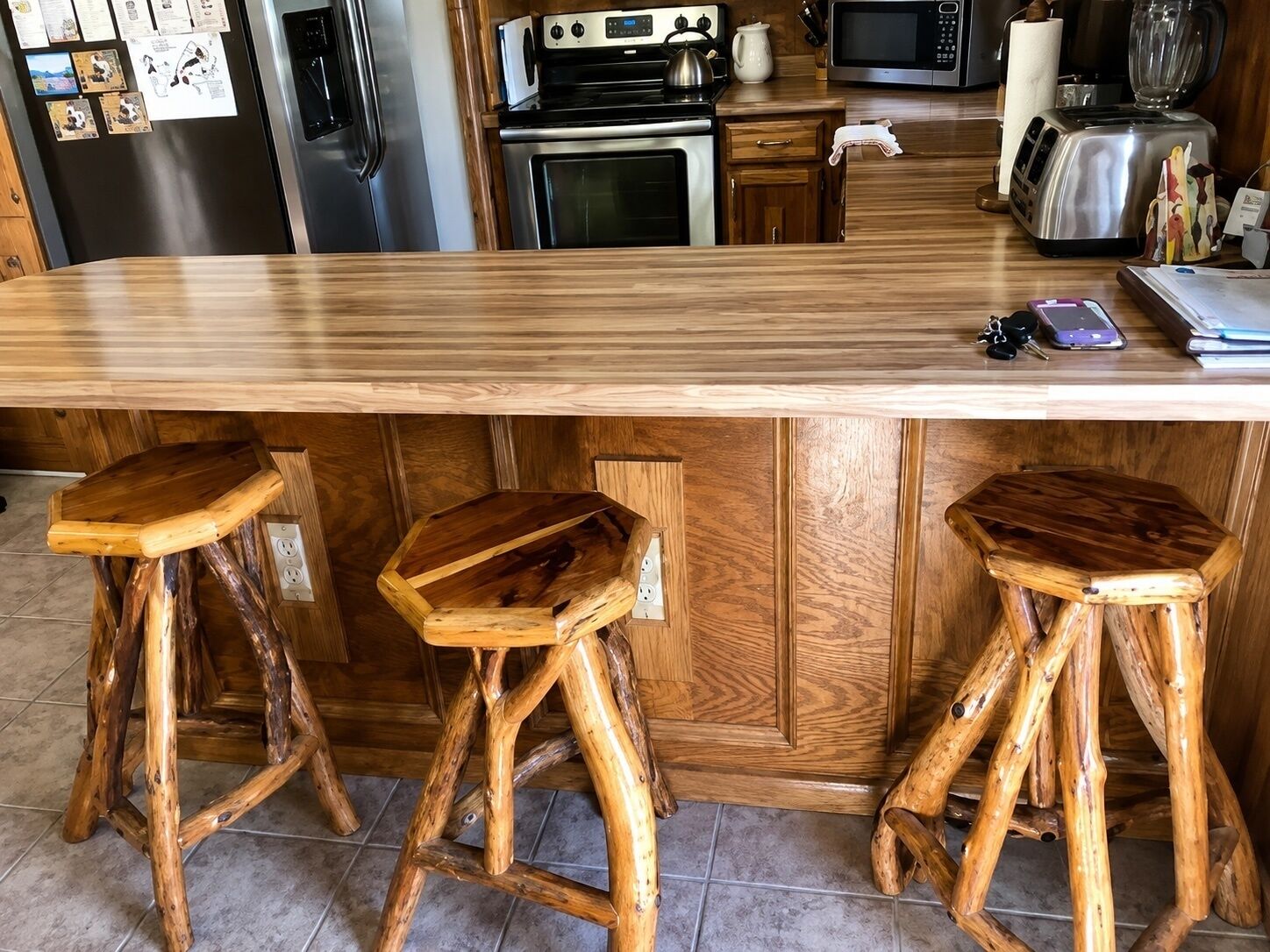Cozinha com balcão de madeira, banquetas, geladeira, fogão, micro-ondas e torradeira.