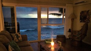 A living room with a large window overlooking the ocean, a sofa, a chair, and a table with a candle. - Oceanfront Penthouse, As Close As You Can Stay To Ocean, Stunning Views, A/C! (Kailua-Kona)