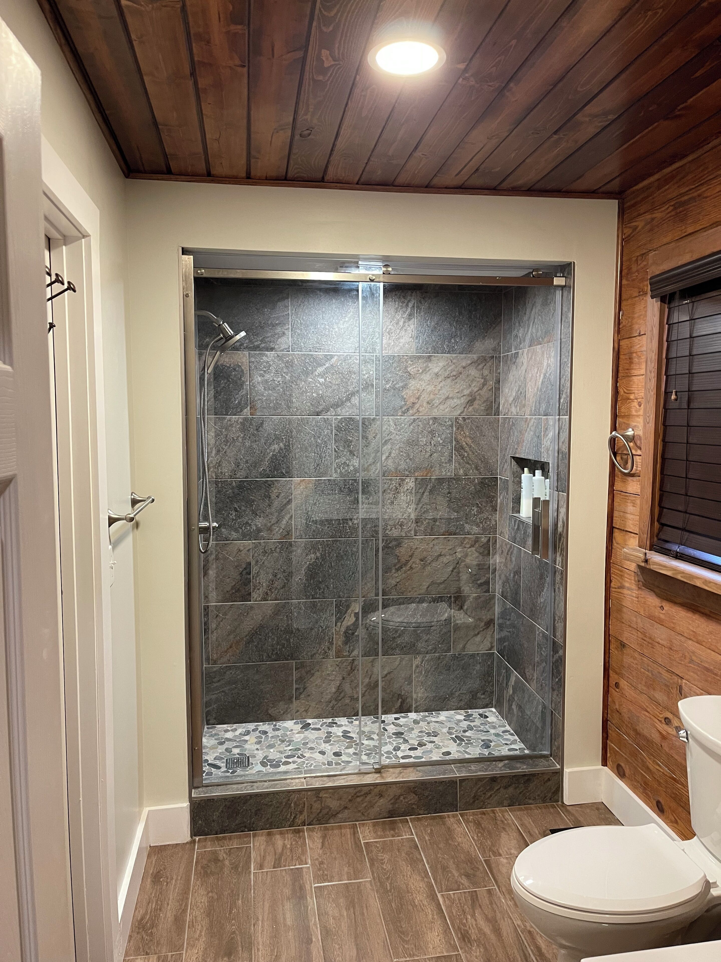 Baño con ducha, inodoro y techo de madera.