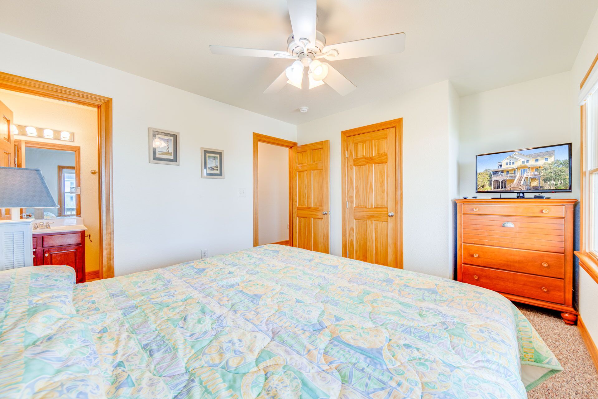 A bedroom with a bed, a ceiling fan, a dresser, and a television.