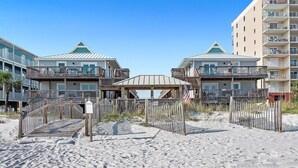 A beachfront hotel with multiple balconies, a covered walkway, and a sandy beach area.