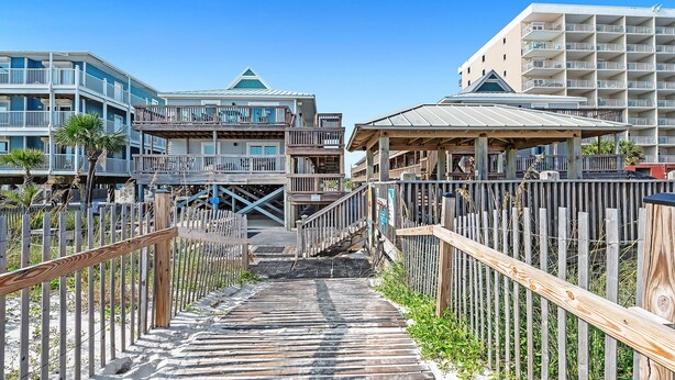 A wooden boardwalk leading to a beachfront hotel with multiple balconies and a covered area.