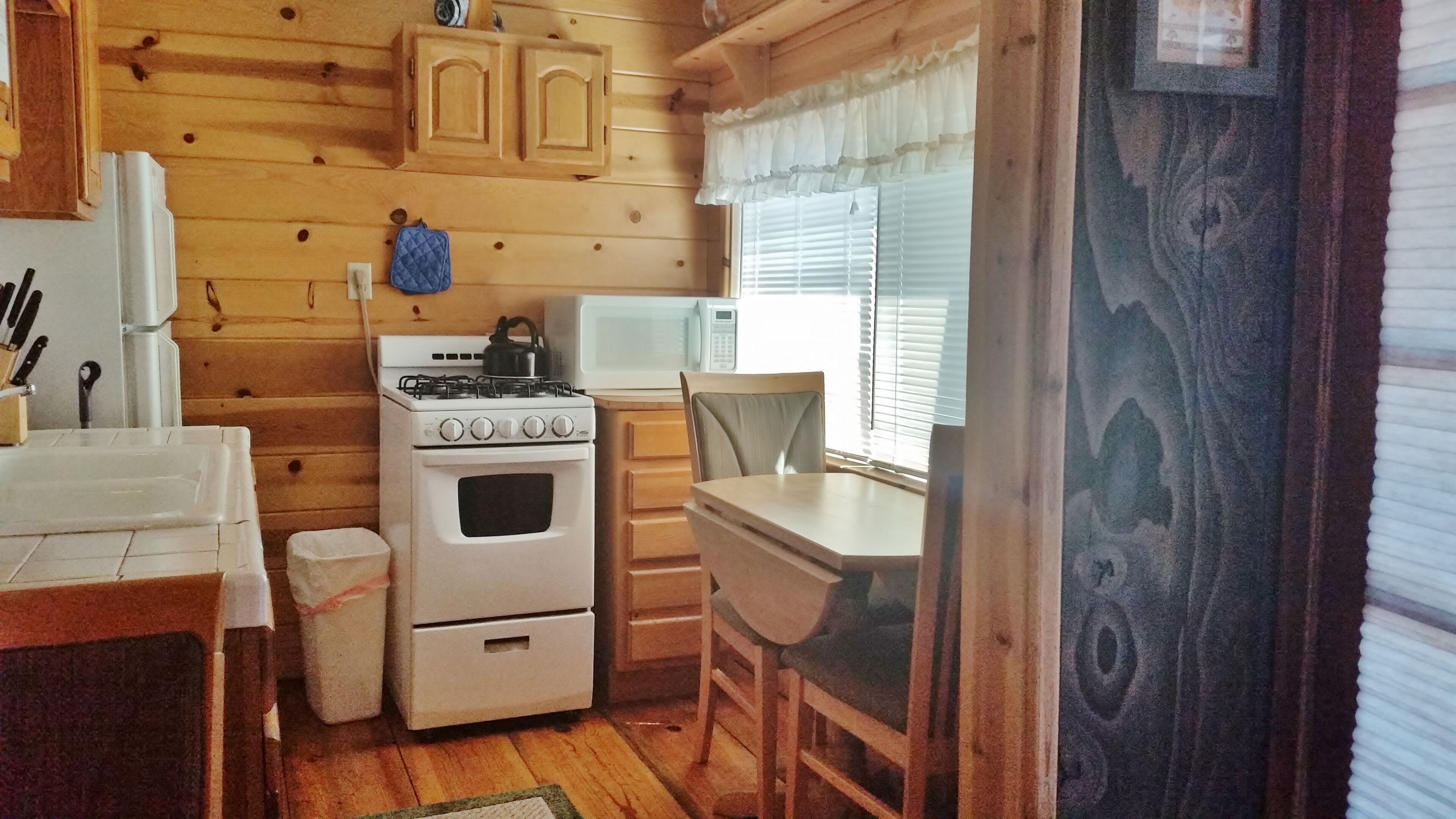 Cocina pequeña con paredes de madera, estufa, microondas y fregadero.