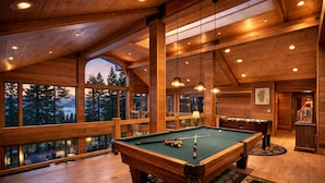 A wooden interior with a pool table, large windows, and a view of trees.
