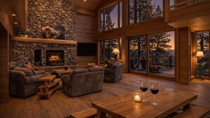 A spacious living area with a stone fireplace, comfortable seating, and large windows offering a view of the outdoors.