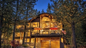 A two-story log cabin with a stone foundation, large windows, and an American flag.