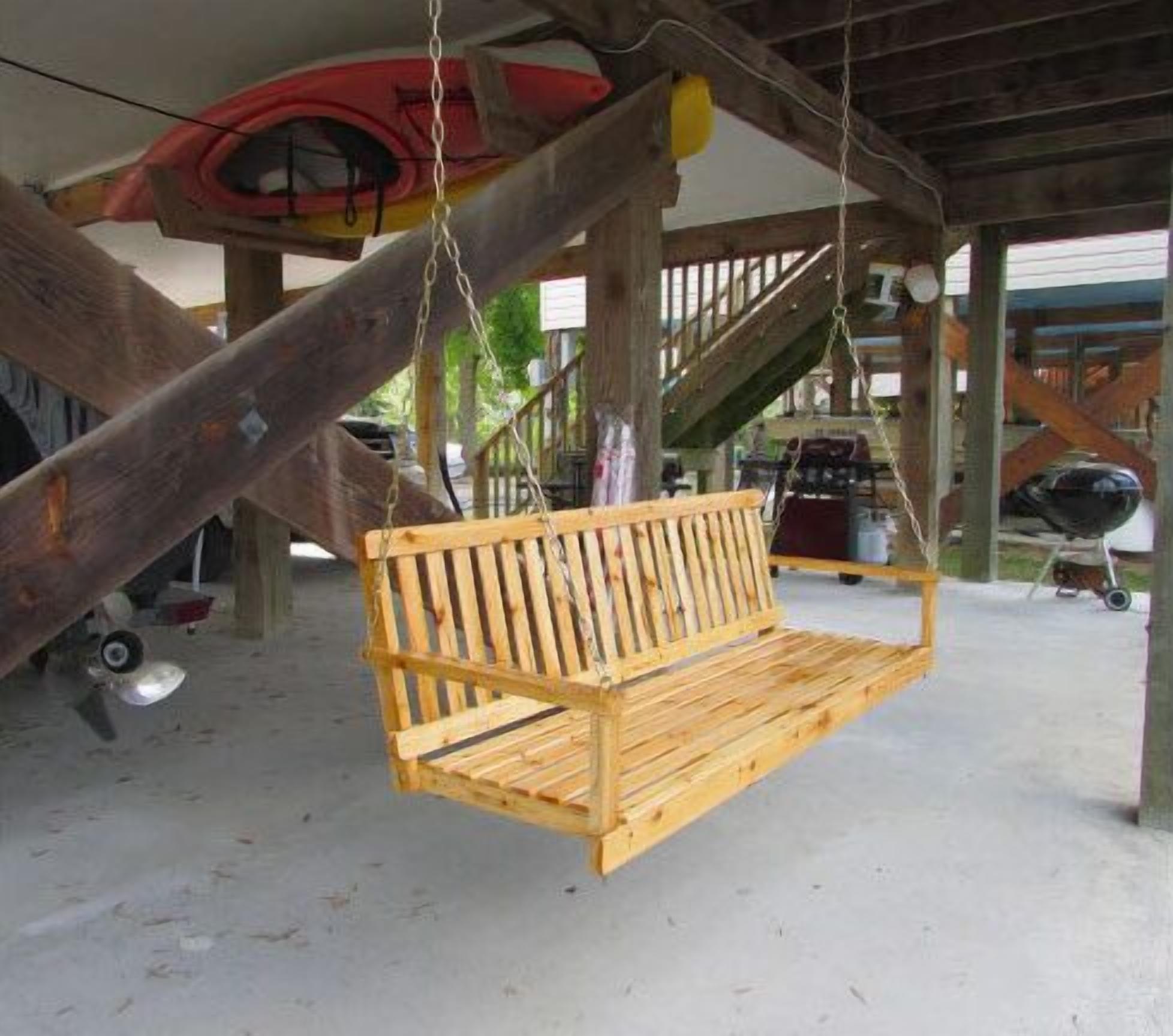A wooden swing suspended from a wooden structure with a kayak and a canoe in the background.