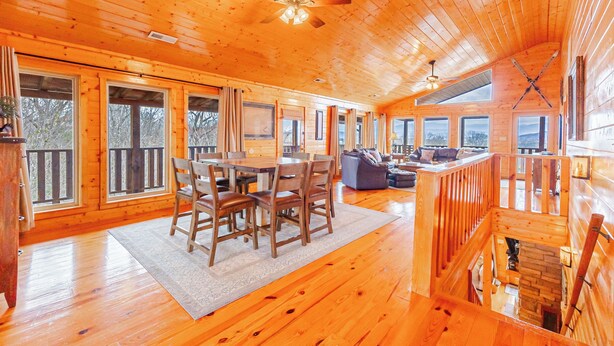 A spacious wooden cabin with a dining area, a living room with a sofa and fireplace, and large windows offering views of the outdoors. - Heavenly View Cabin (Sevierville)