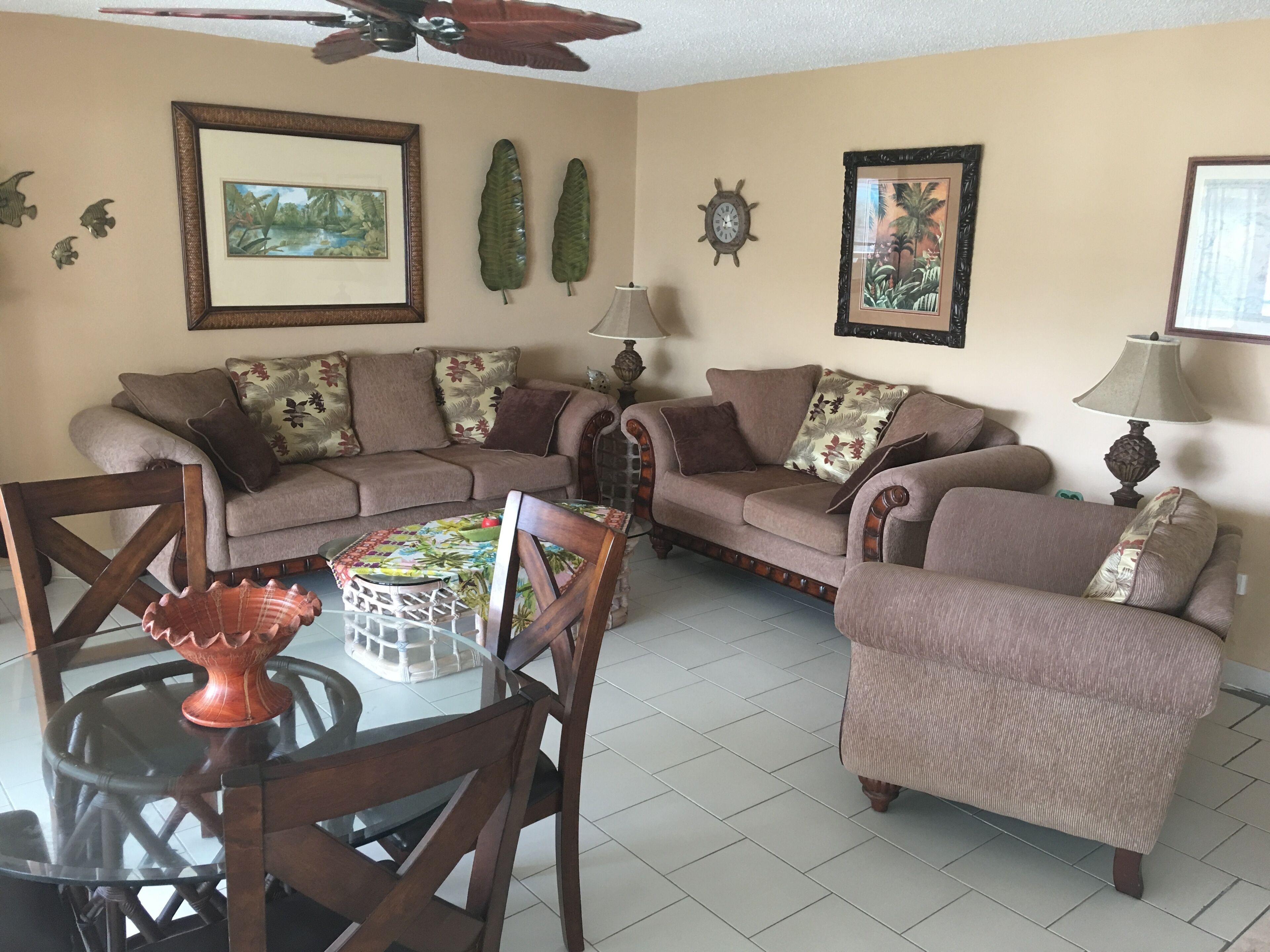 A living room with a sofa set, a dining table with chairs, and a ceiling fan.
