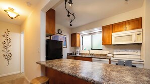 Una cocina con encimeras de granito, armarios de madera, microondas y estufa.