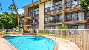 Un hotel de varios pisos con piscina, mobiliario exterior y un patio amurallado.