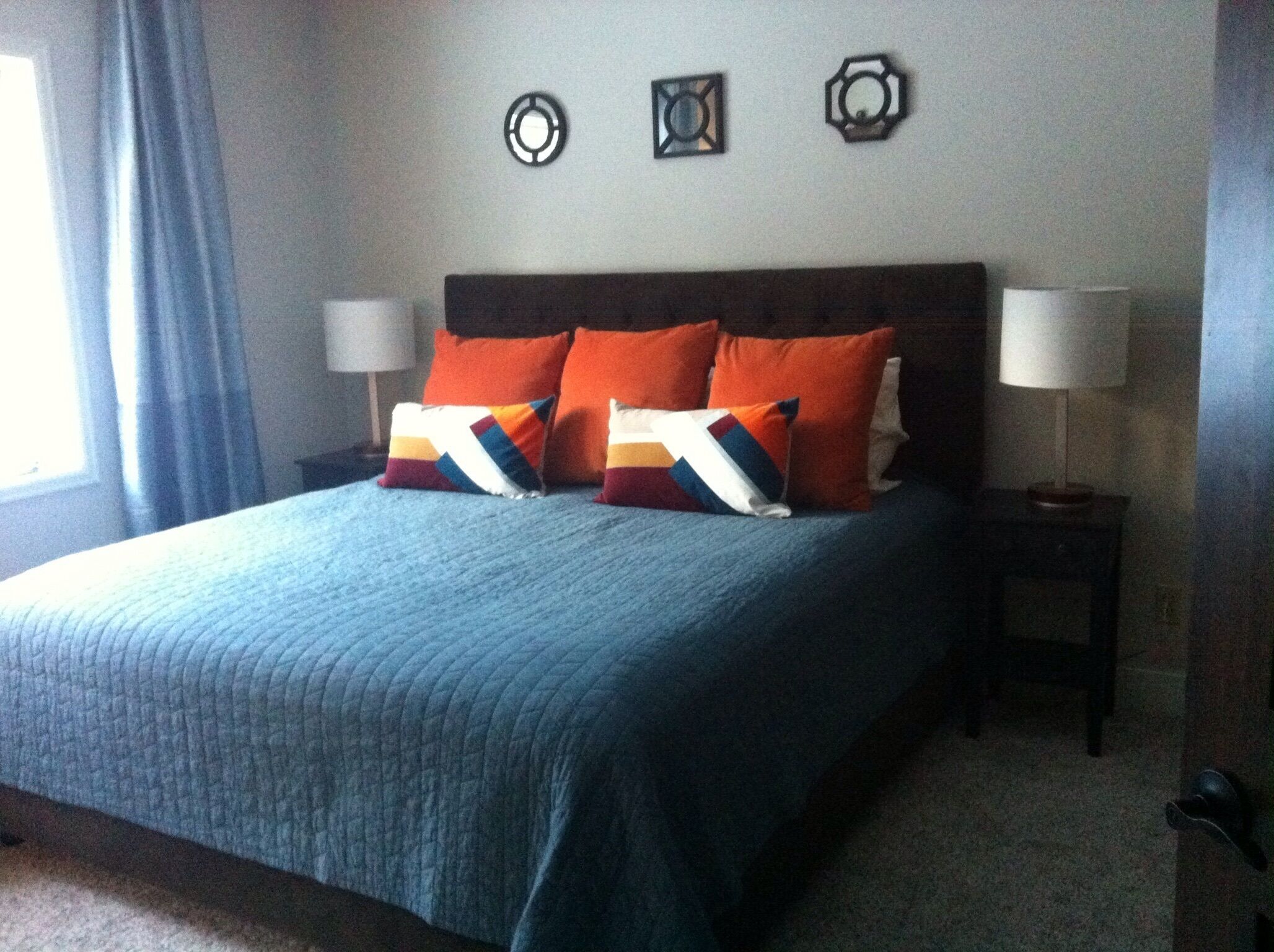 A neatly made bed with a blue quilt, two orange pillows, and two matching nightstands with lamps.