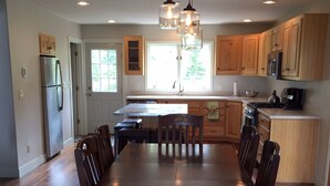 A modern kitchen with wooden cabinets, a central island, and a dining table with chairs. - Ski In/Out, Walk To Trails & Town, 4 Bdr Townhome. (Breckenridge)